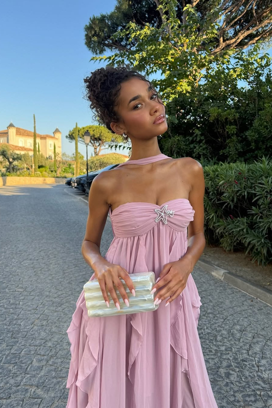 Pink ruched maxi dress with strapless sweetheart neckline and halter tie, featuring a starfish brooch and ruffled skirt details.