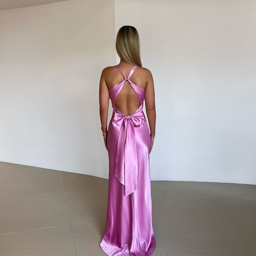 Back view of a fuchsia pink satin maxi dress with a large bow detail and criss-cross straps, ideal for an evening event.