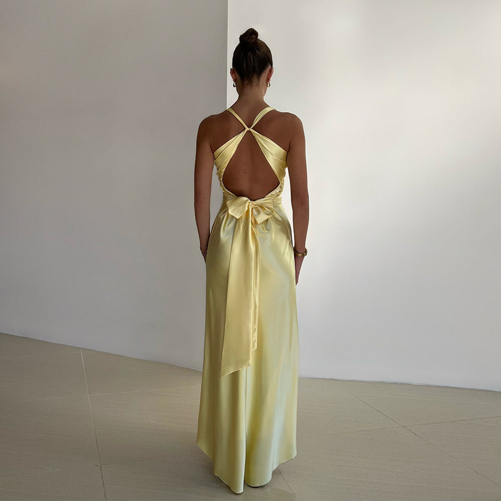 Back view of a yellow satin maxi dress featuring a large tie-back bow and open back with criss-cross straps.
