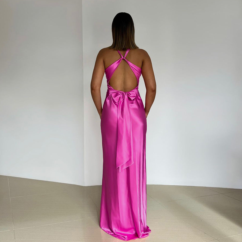 Back view of a fuchsia pink satin maxi dress with an open back, criss-cross straps, and a large bow tie closure.