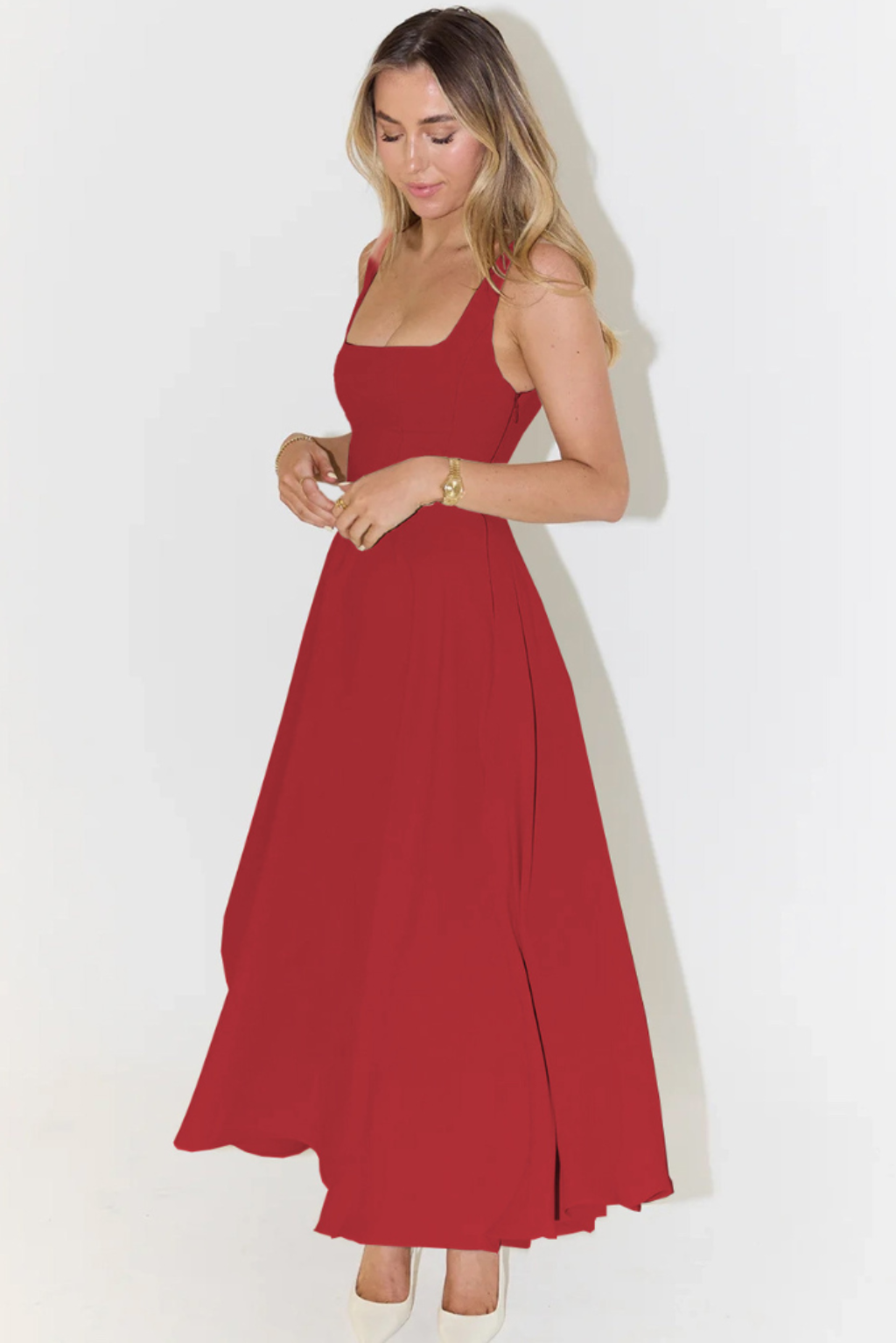 Side view of a red A-line midi dress with a flowing skirt and a subtle side slit, paired with white heels.