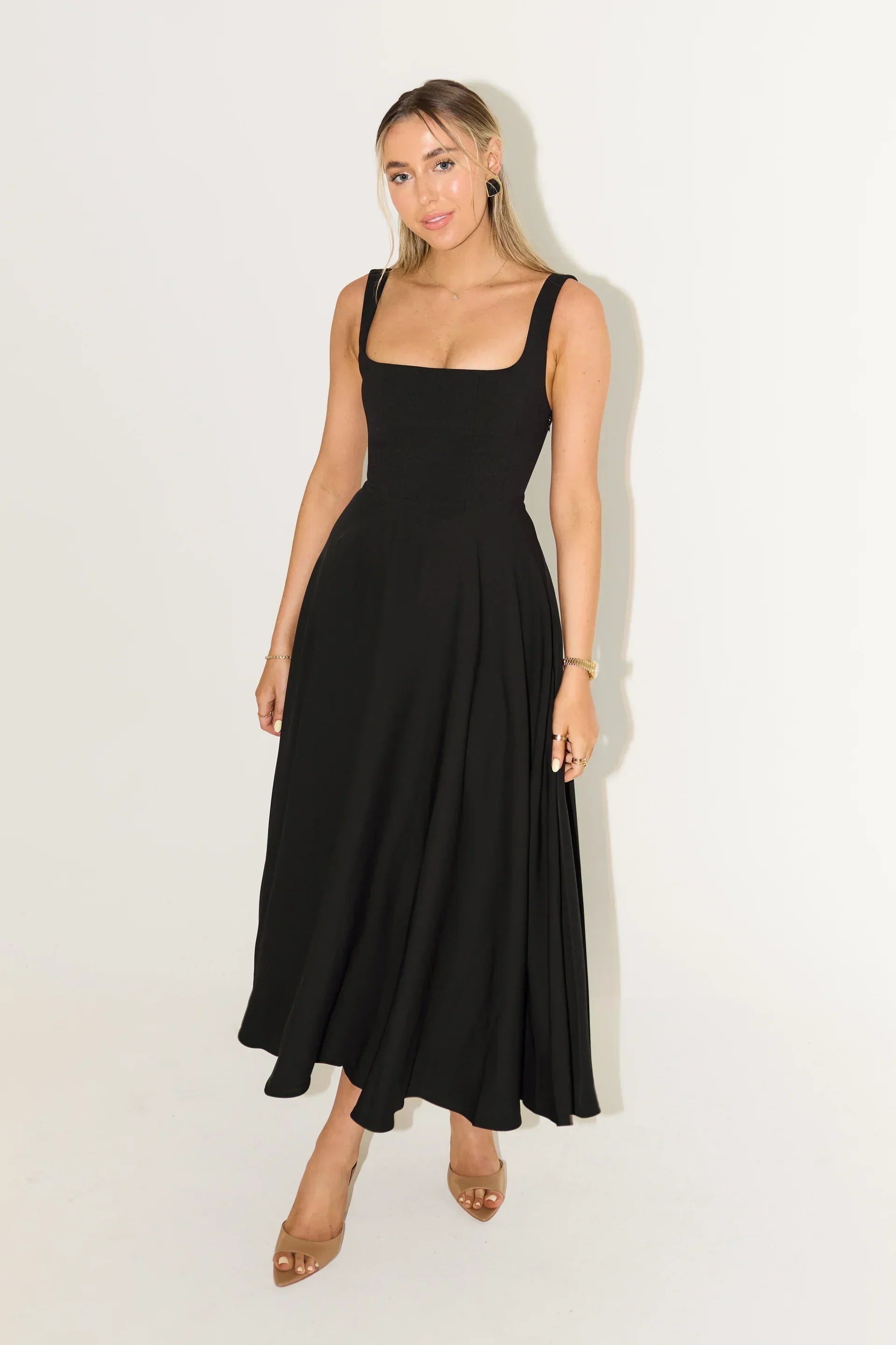 Full view of the Eliza A-line midi dress in black, with a flowing skirt and square neckline, paired with nude heels.