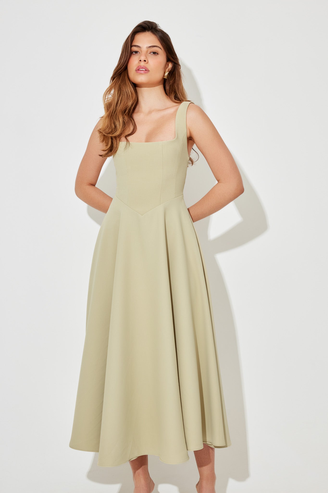 Front view of the Eliza A-line midi dress in light sage green, with hands clasped in front, showcasing the V-shaped waistline.