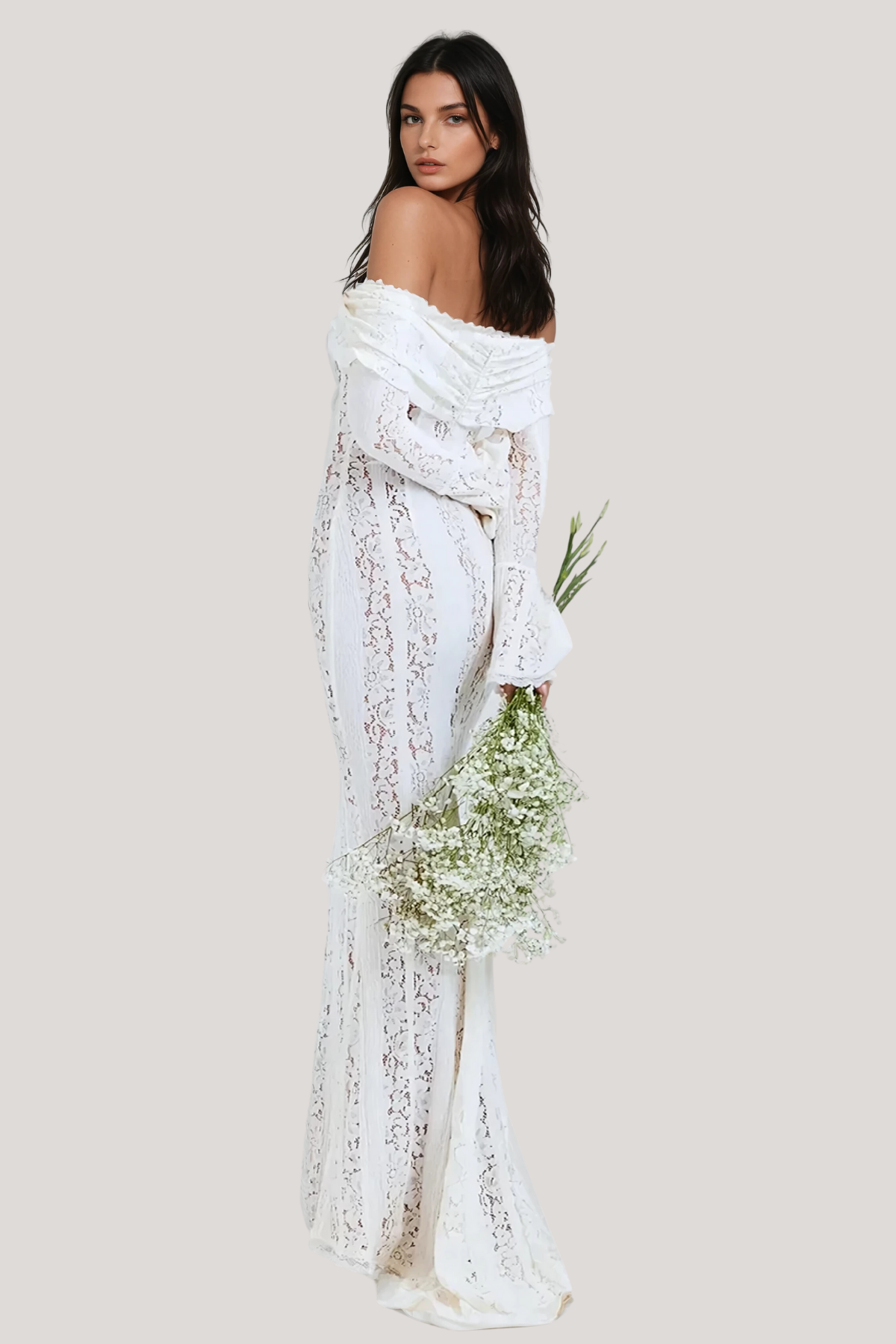 Back view of a white lace maxi dress with off-the-shoulder detail and long sleeves, holding a bouquet of white flowers.