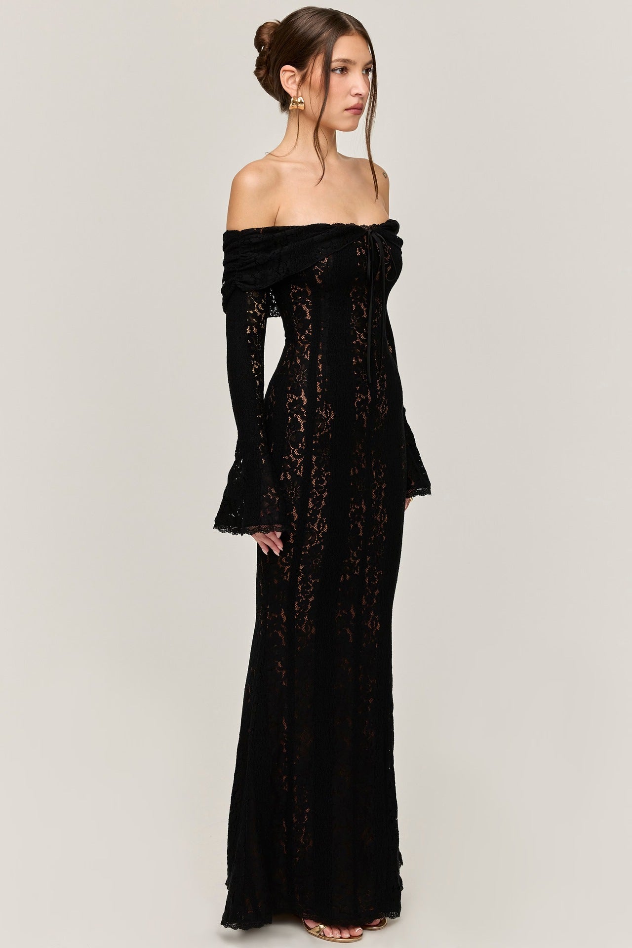 Side profile of a black lace maxi dress, showing the off-the-shoulder neckline, long bell sleeves, and fitted silhouette.