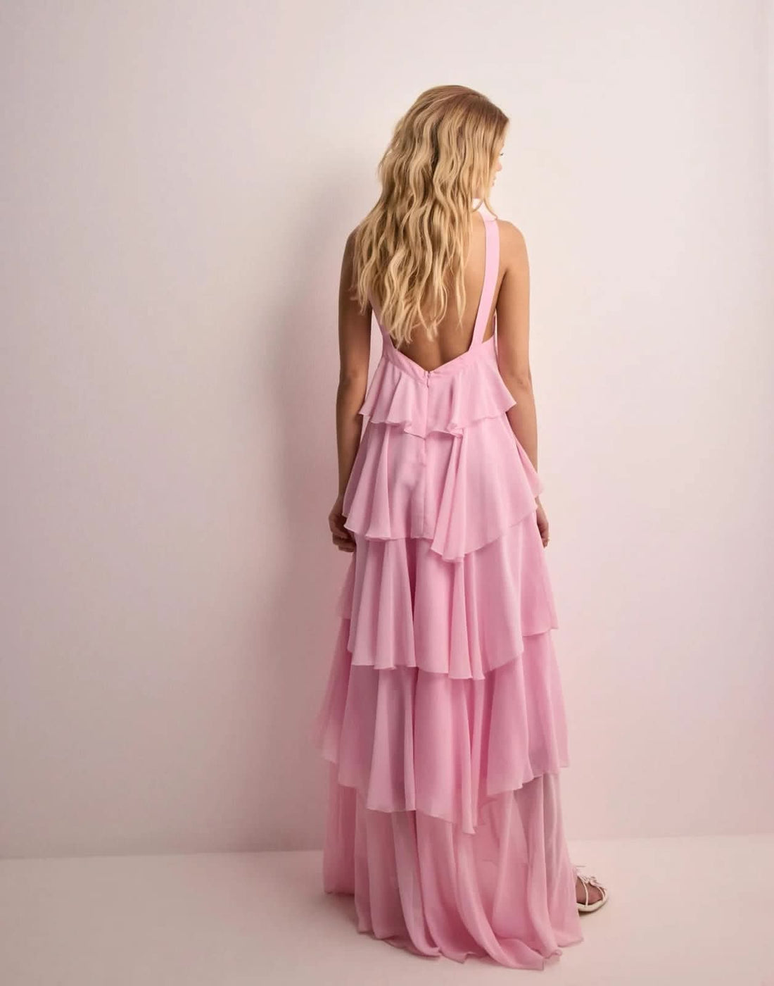 Full-length view of a woman wearing a light pink ruffle maxi dress with a halter neckline and tiered skirt.