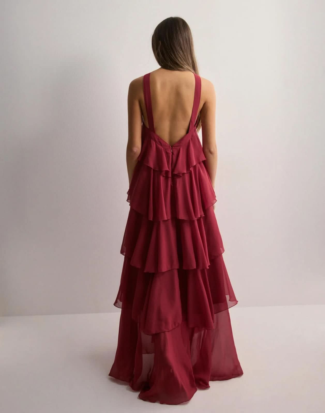 Back view of a woman wearing a deep red Eloise ruffle maxi dress, showcasing the tiered skirt and low back.