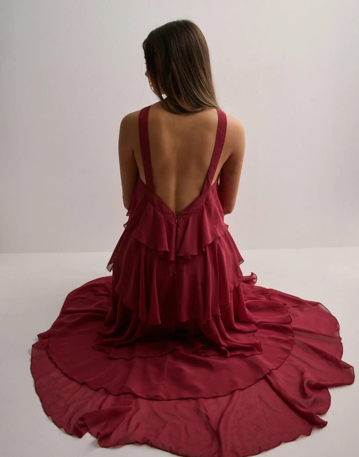 Woman sitting on the floor, seen from behind, in a deep red ruffle maxi dress with flowing tiered skirt.