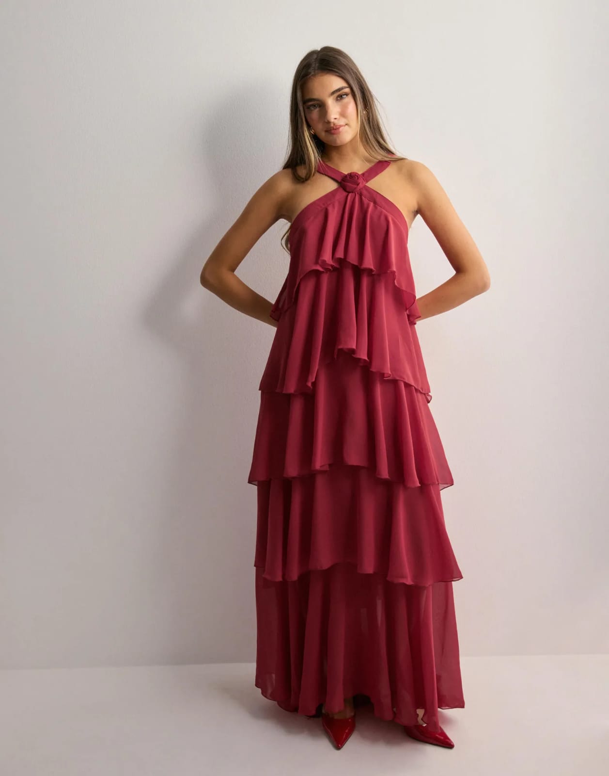 Full-length view of a woman standing in a deep red ruffle maxi dress with a halter neckline and layered skirt.