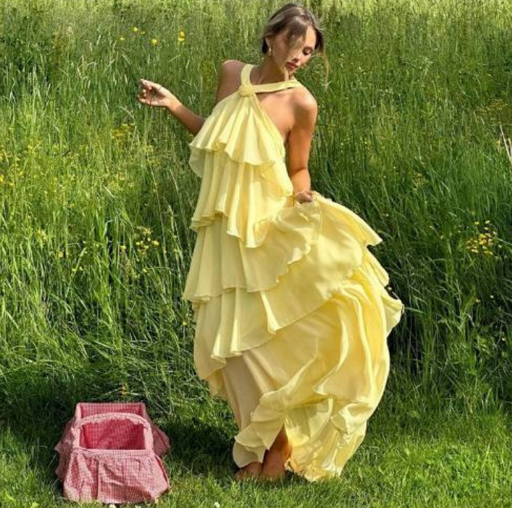 Woman walking through a grassy field in a flowing yellow ruffle maxi dress with a halter neck.