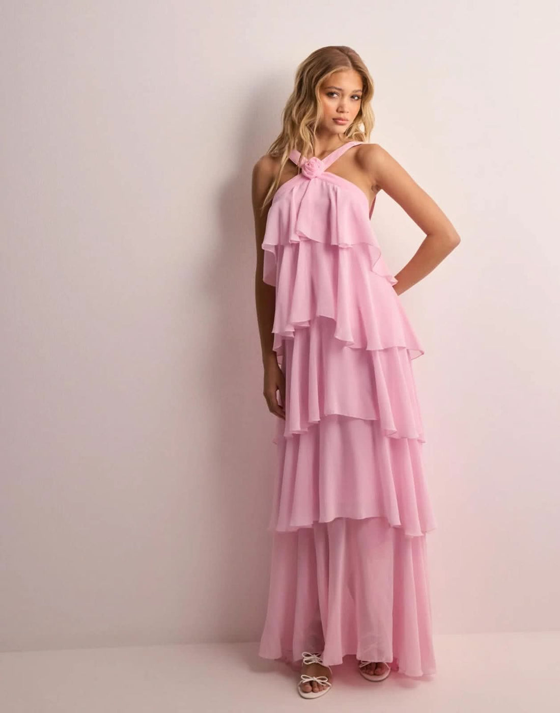 Full-length view of a woman wearing a light pink ruffle maxi dress with a halter neckline and tiered skirt.