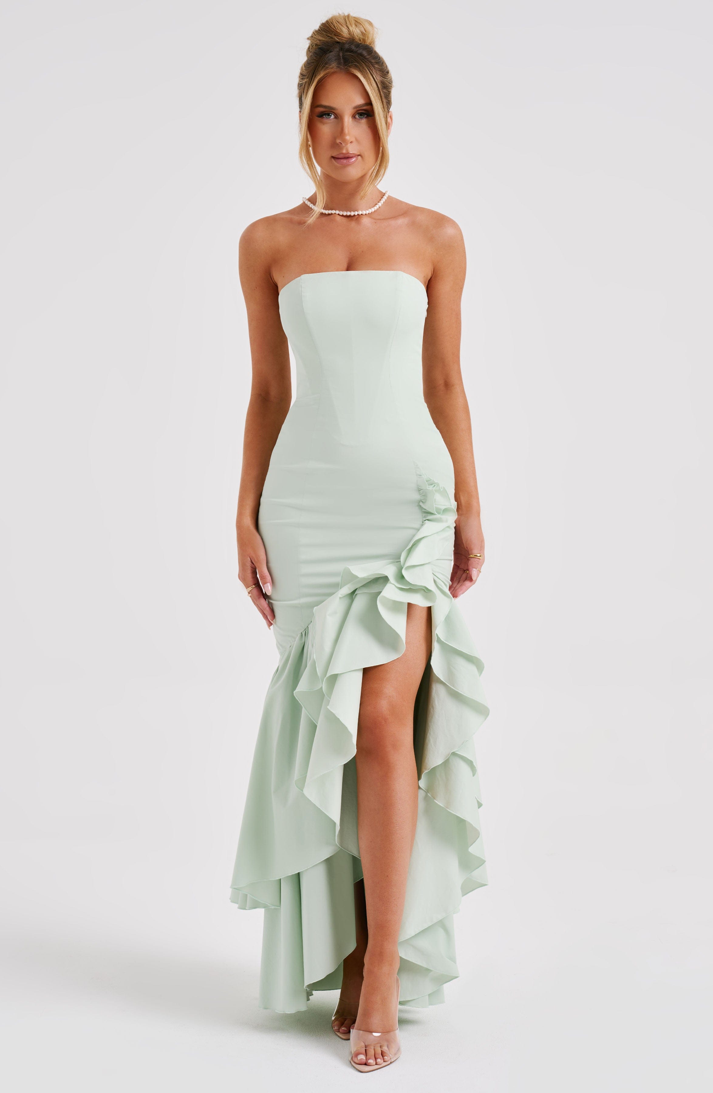 Full-length view of a strapless mint green maxi dress with a ruffled high-low hem and side slit.