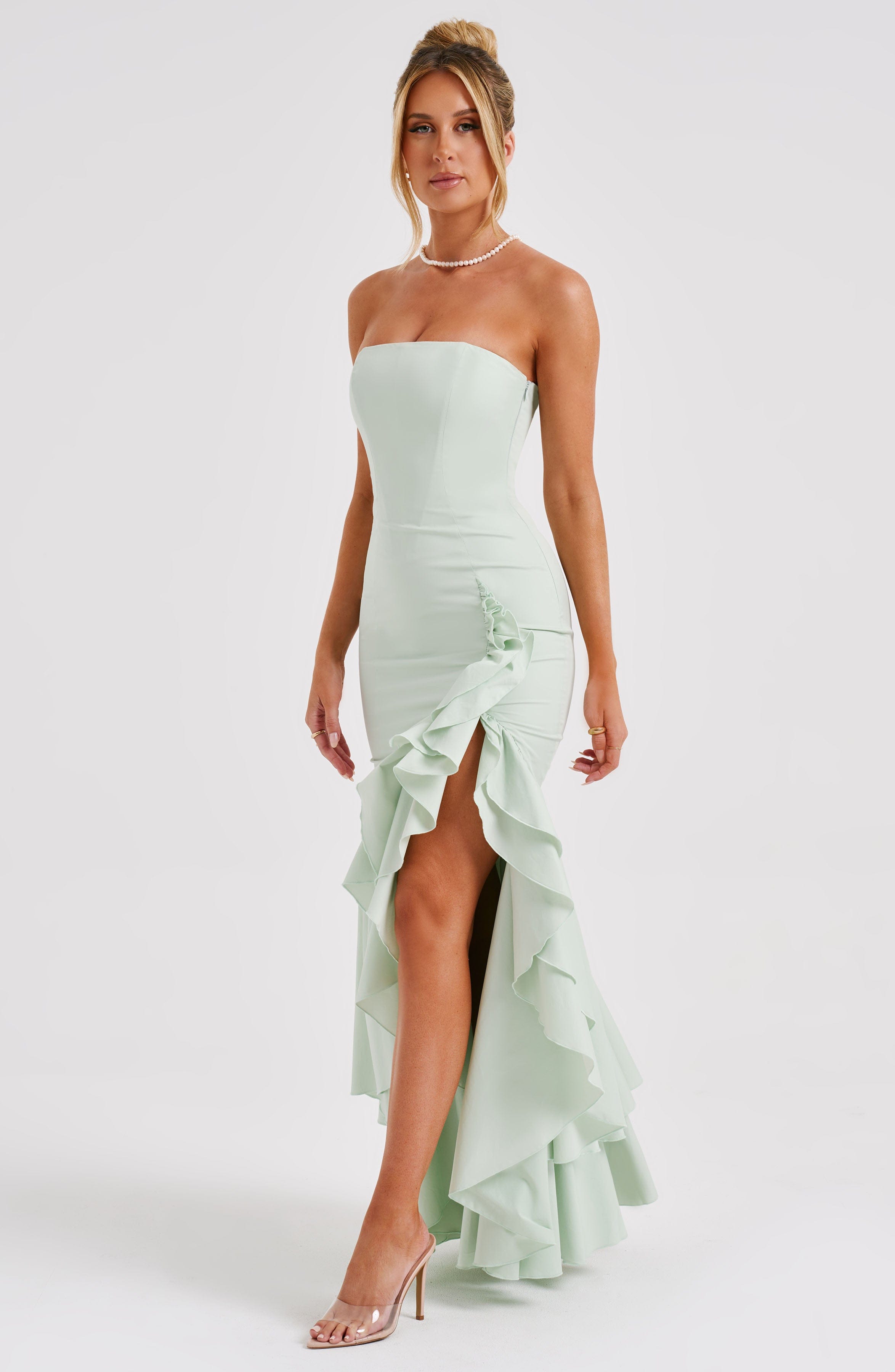 Angled view of a mint green strapless maxi dress featuring a dramatic ruffled hem and leg slit.