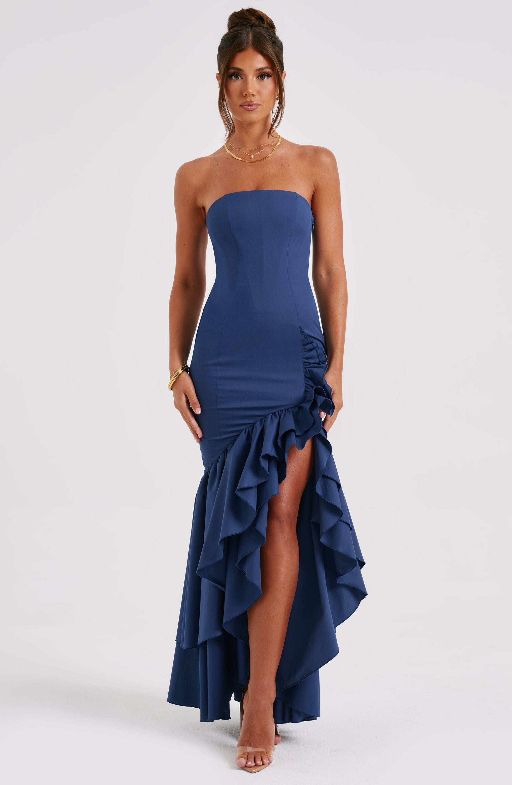 Front view of a navy blue strapless maxi dress with a ruffled high-low hem and side leg slit.