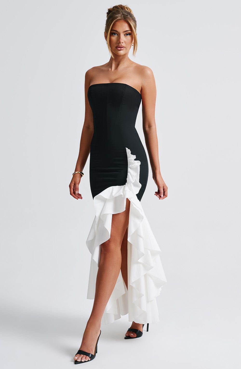 Angled view of the black and white Emily Ruffle Maxi Dress, emphasizing the high-low hem and flowing white ruffles.