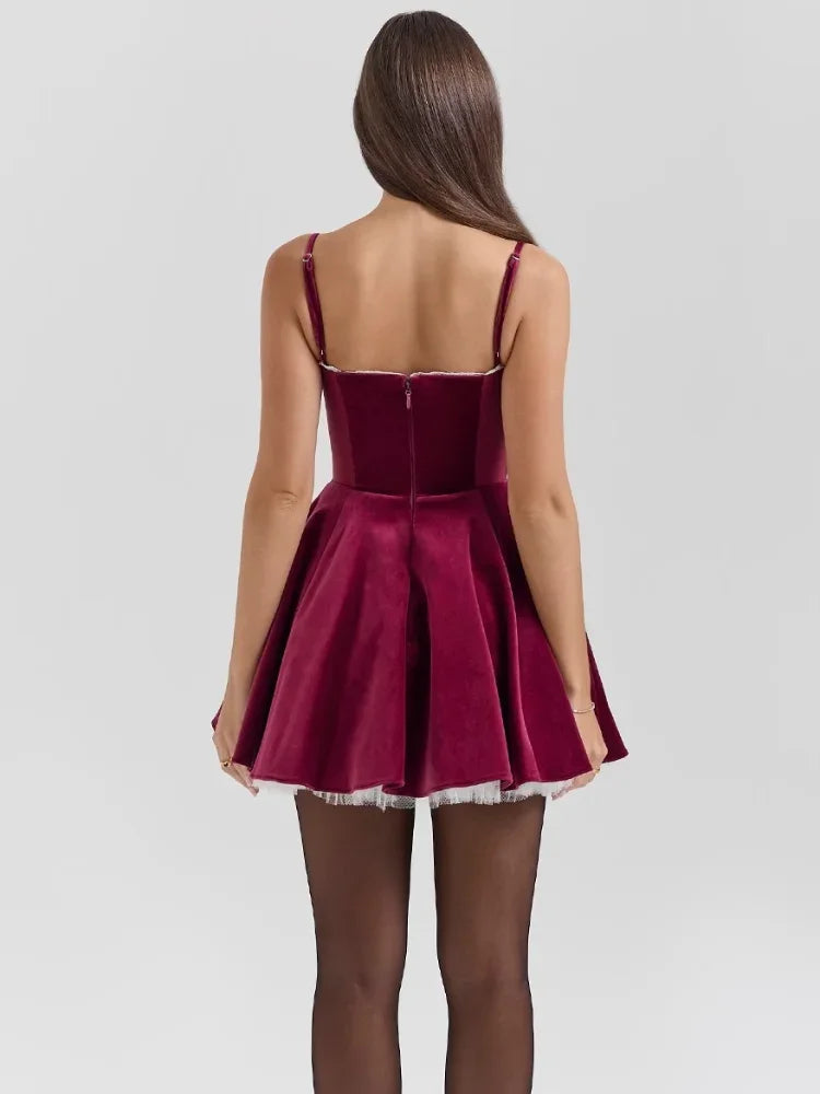 Back view of a dark red velvet mini dress with thin straps, a structured bodice, and a full skirt with white tulle peeking out, worn with black tights.