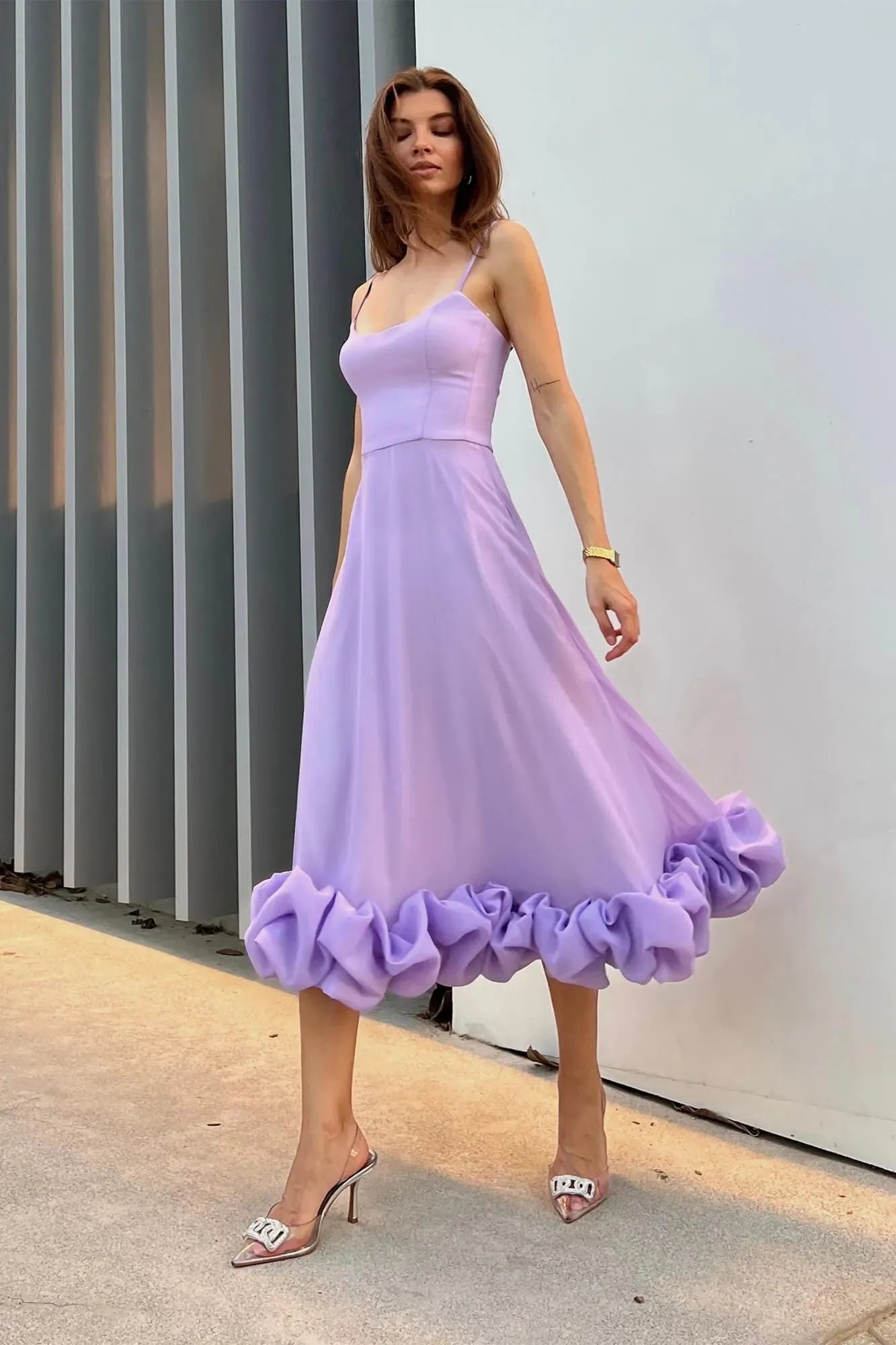 Lavender Emmeline ruffle midi dress with spaghetti straps and voluminous tiered hem, paired with clear heels.