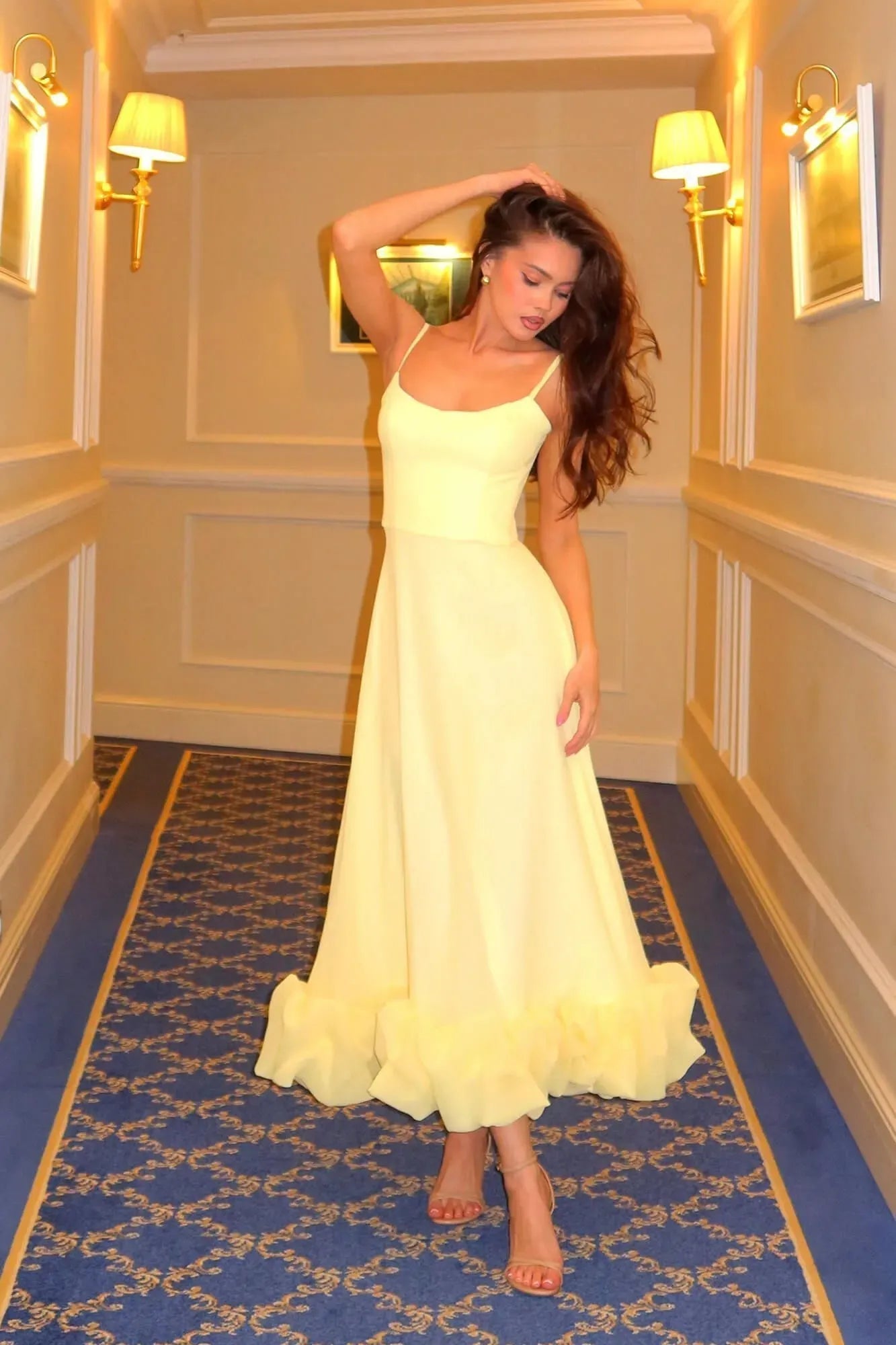 Full length view of a light yellow Emmeline ruffle midi dress with delicate spaghetti straps and a tiered hem.