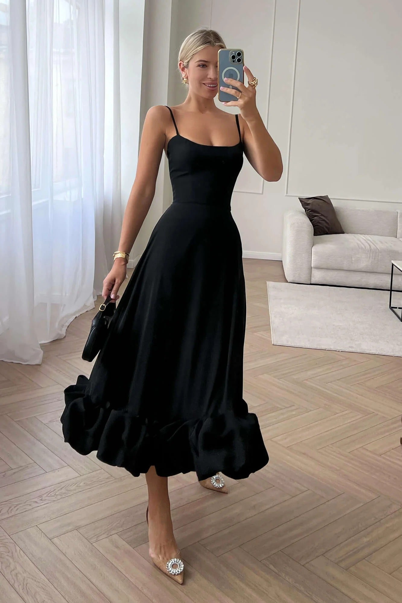 Black Emmeline ruffle midi dress with spaghetti straps and a full, tiered ruffle hem, worn with embellished heels.