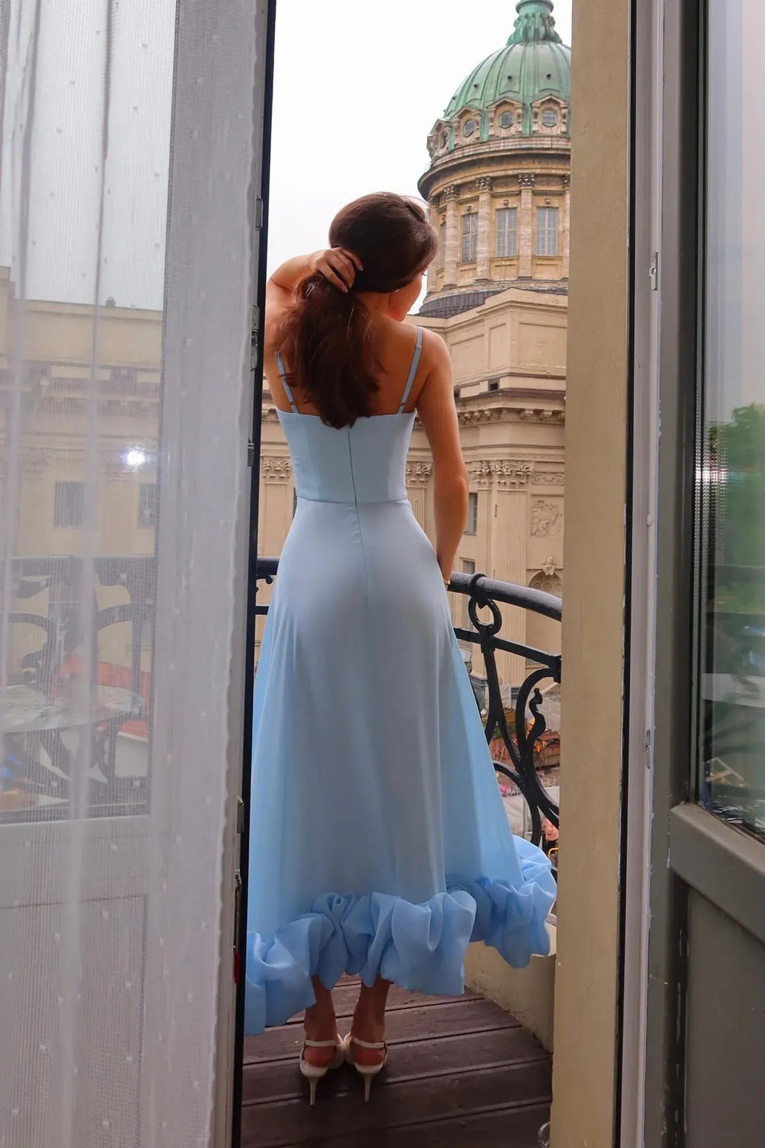 Light blue midi dress with spaghetti straps and ruffled hem, worn with white heels on a balcony.