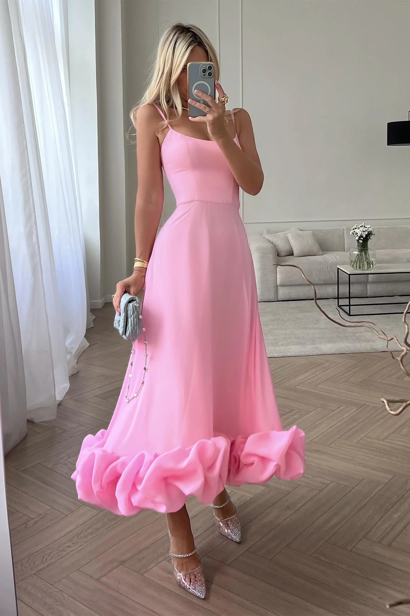 Pink midi dress with thin straps and a large ruffled hem, paired with sparkly pointed-toe heels.