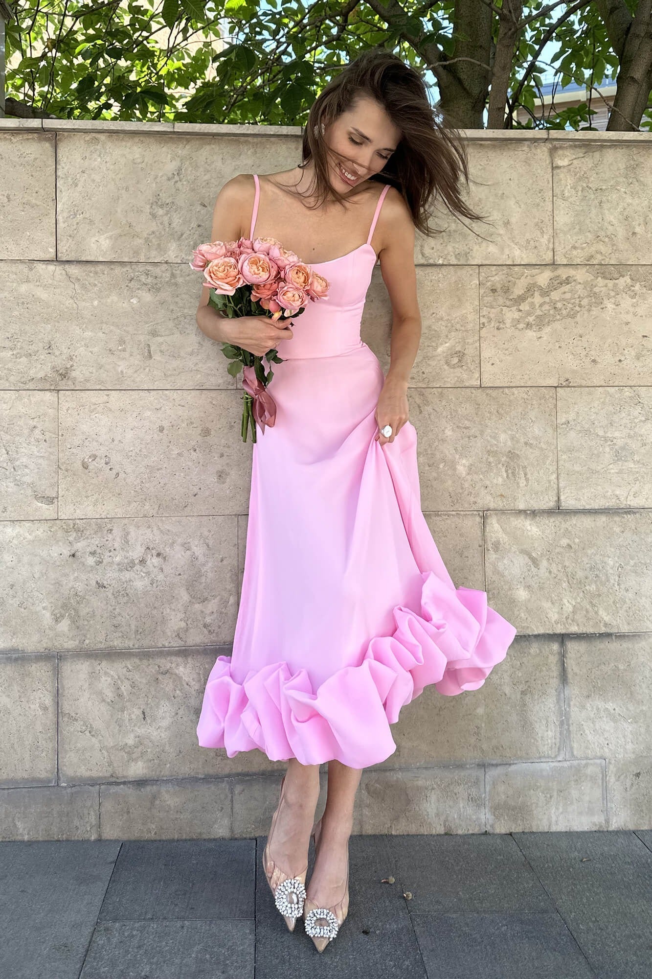 Pink midi dress with spaghetti straps and a ruffled hem, with a bouquet of pink roses, wind blowing hair.