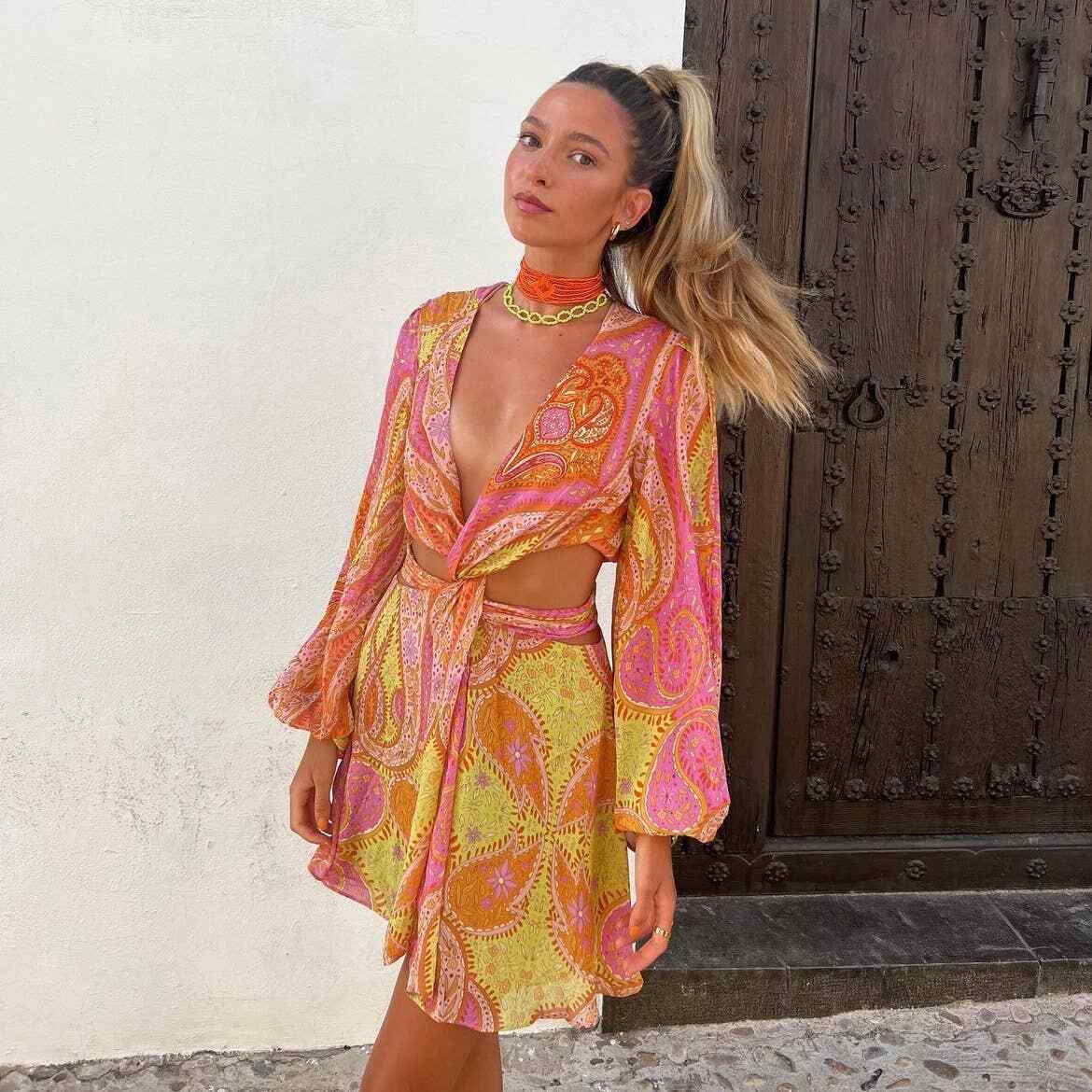 Front view of a woman wearing a vibrant paisley mini dress with long billowy sleeves and a twisted front detail for women