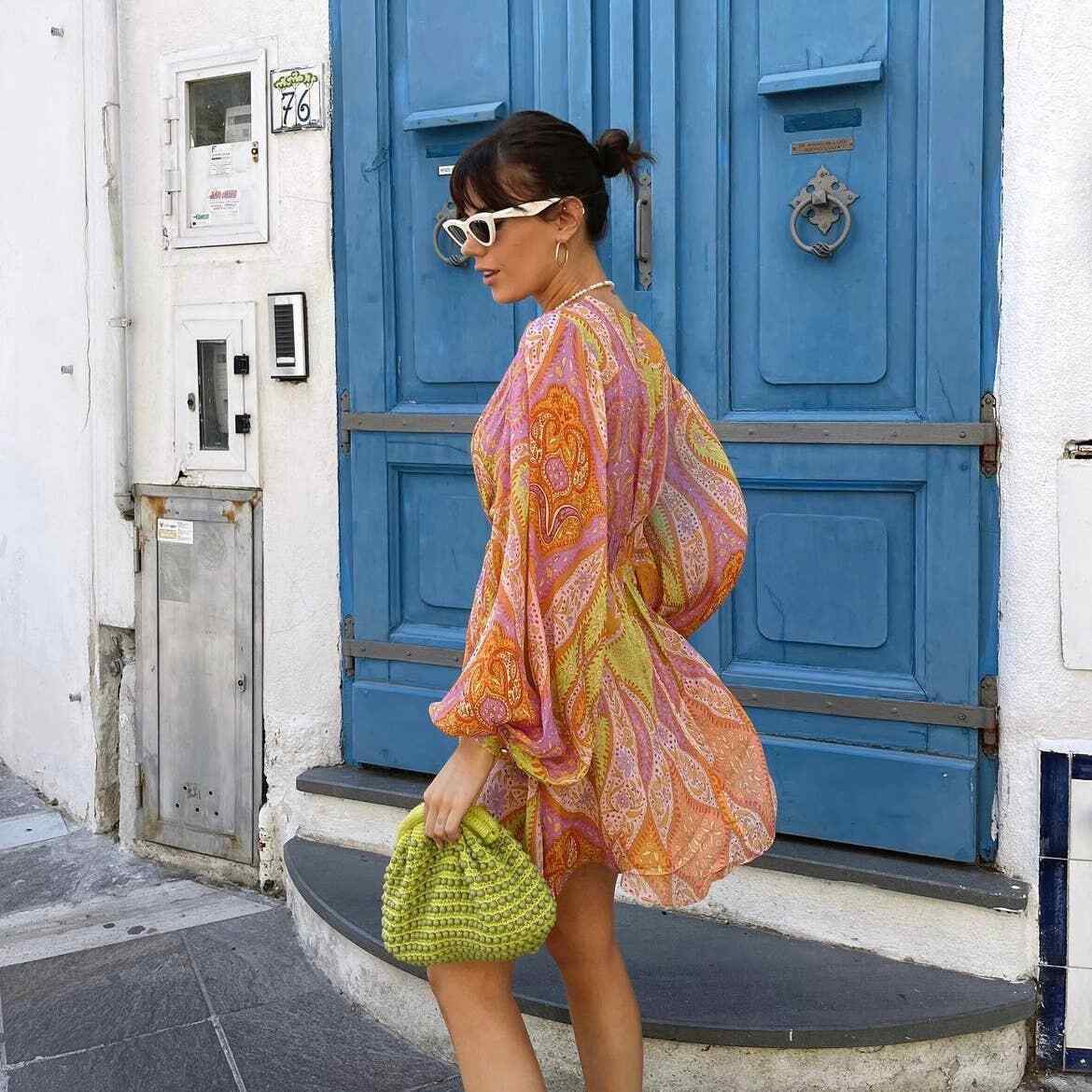 Side profile of a woman walking in a flowing paisley print mini dress with long sleeves and cutout details for women