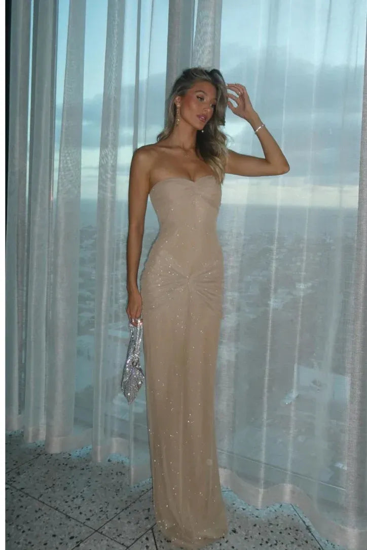 Blonde woman standing in a champagne Estrella Mesh Maxi Dress, strapless with a twisted waist detail.