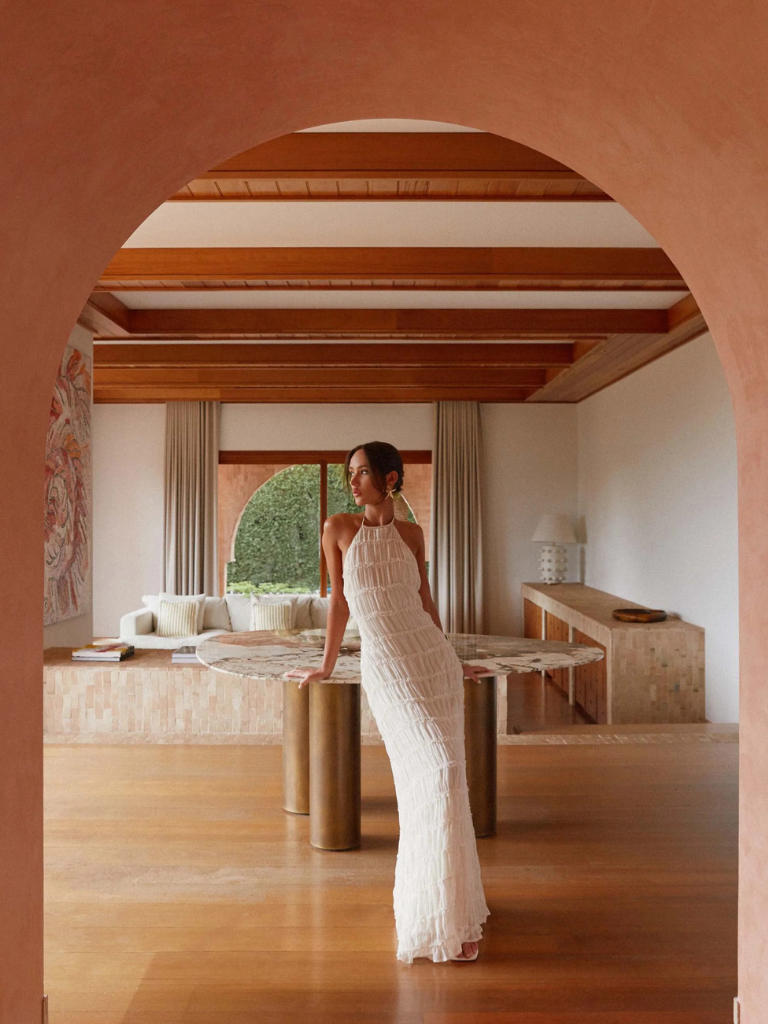 Everly textured maxi dress in off-white, featuring a halter neck and ruched detailing, styled on a model leaning against a pink wall.