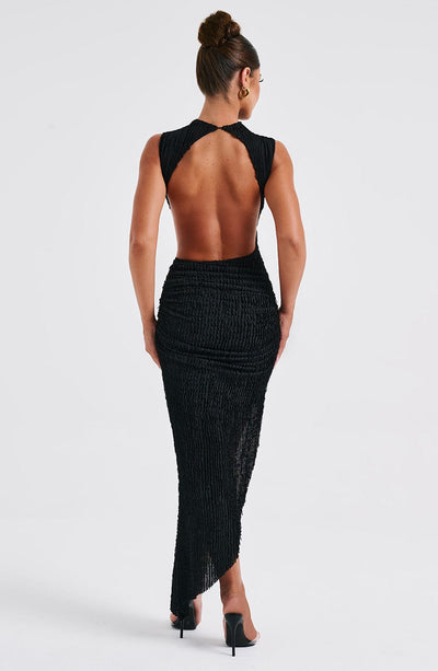 Back view of the black textured maxi dress, highlighting the open back design and the elegant drape of the fabric.