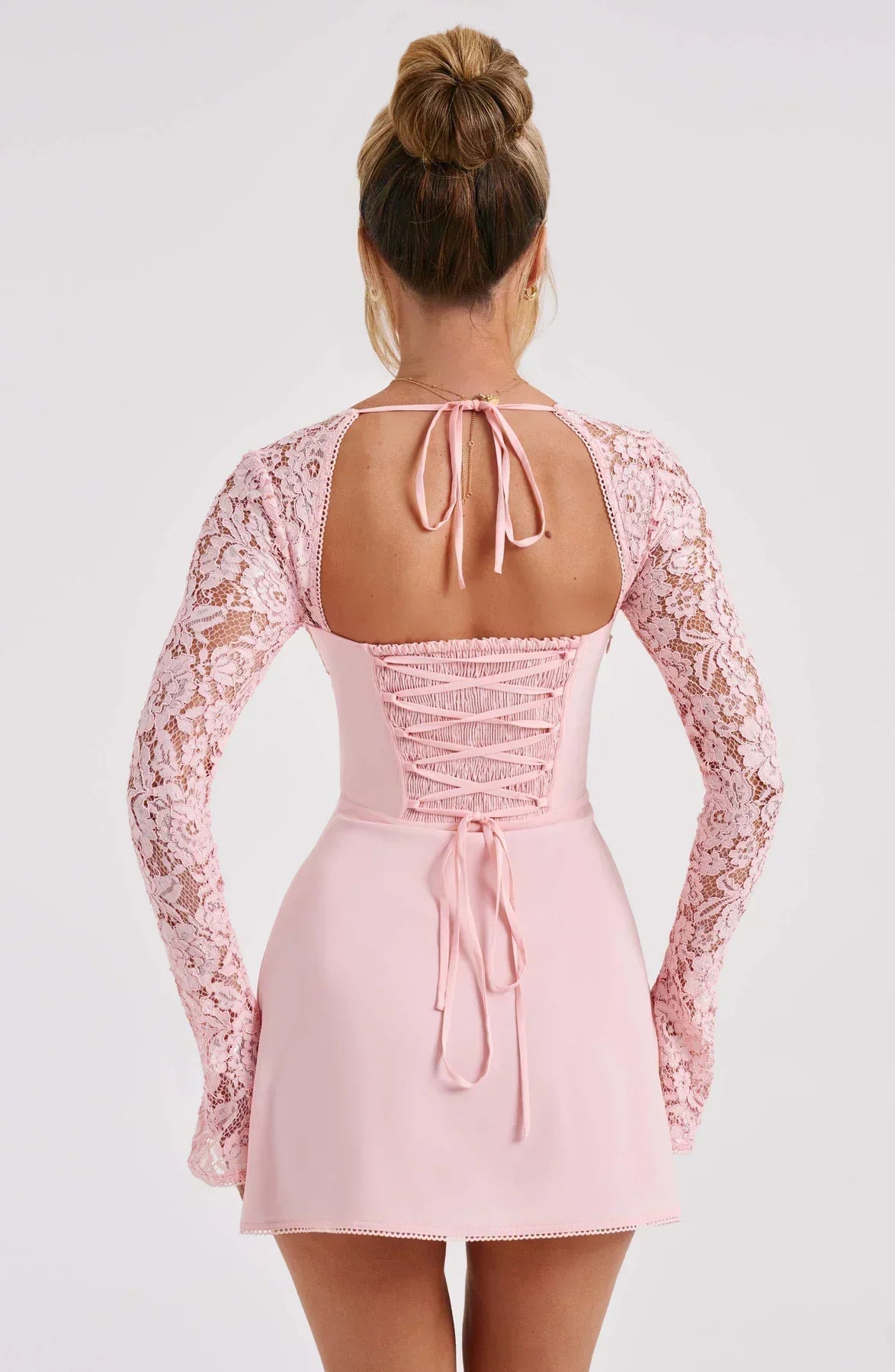 Back view of a light pink mini dress with long lace sleeves and a crisscross corset-style back with tie details.