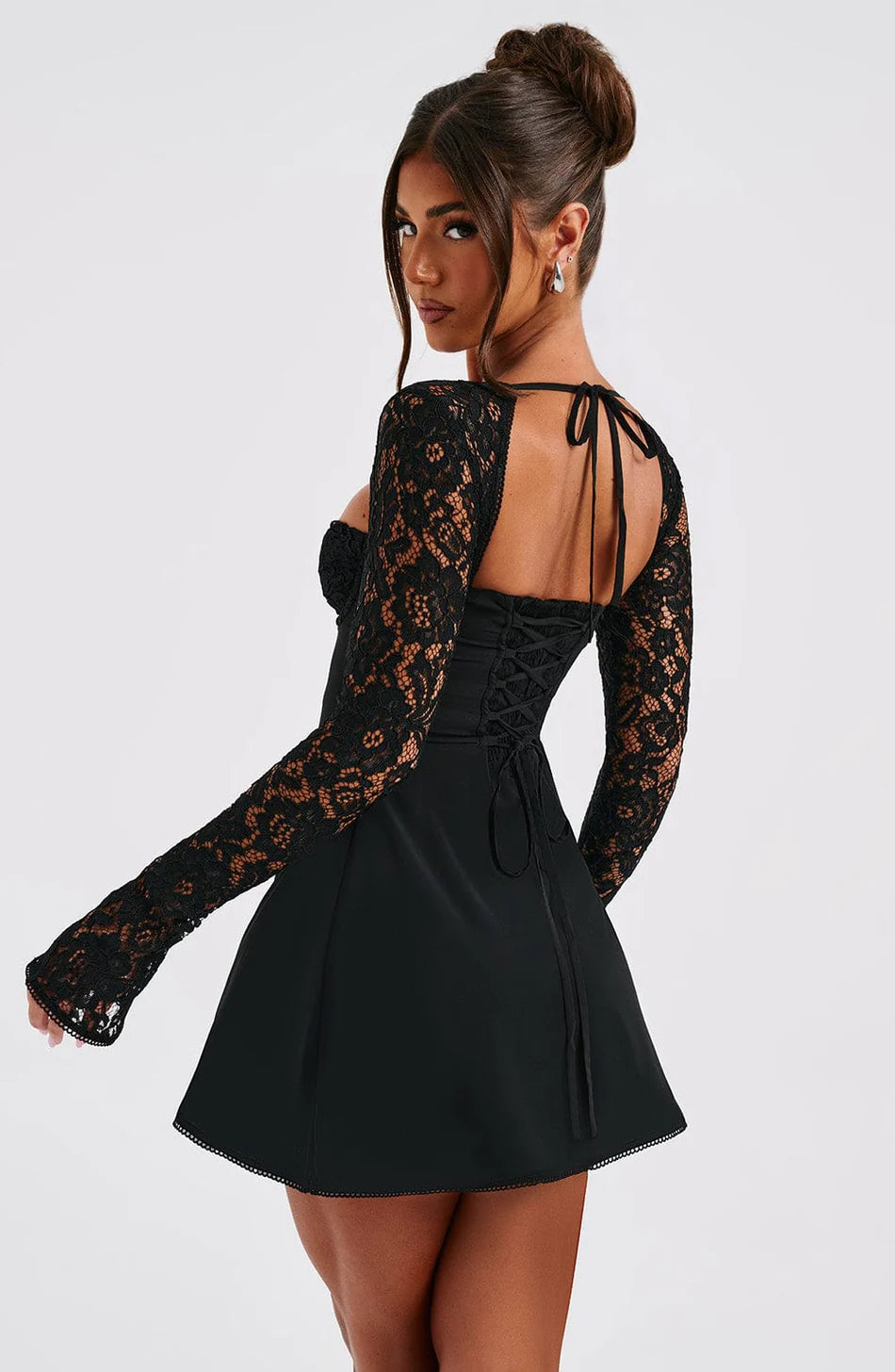 Three-quarter back view of a black mini dress with sheer long lace sleeves and a tie-up corset back, showing the flared skirt.