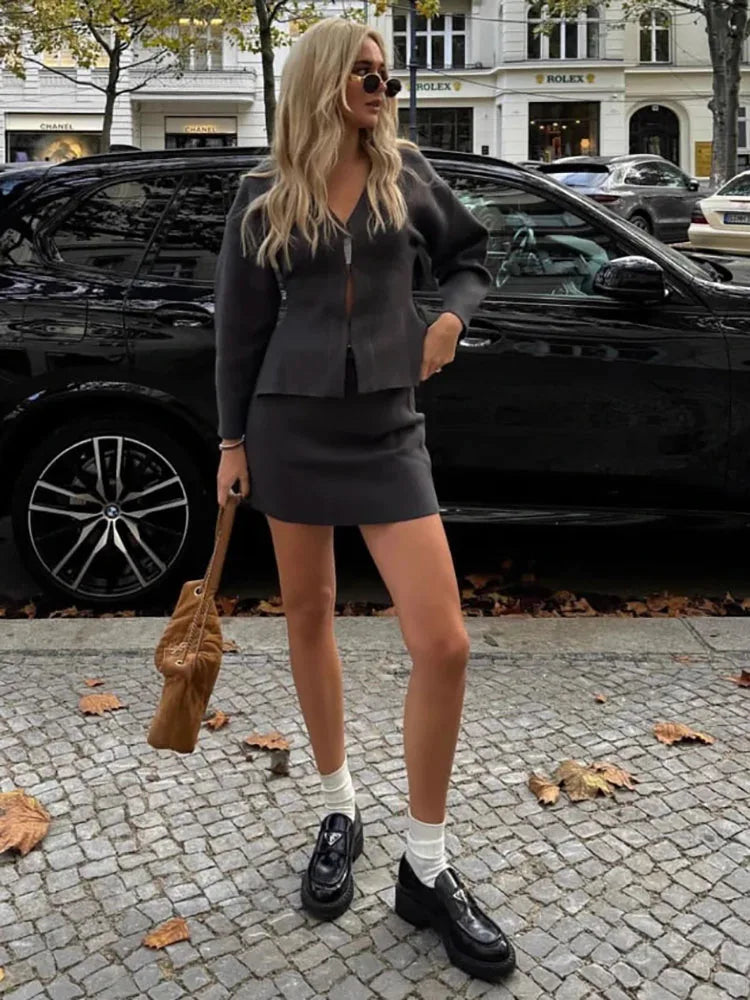 Charcoal grey knit mini skirt and matching v-neck cardigan with long sleeves, paired with black loafers and white socks.
