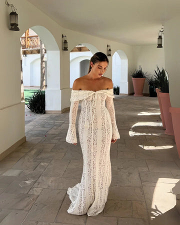 Off-the-shoulder white lace maxi dress with long bell sleeves and a tie-front detail, walking on a patio.