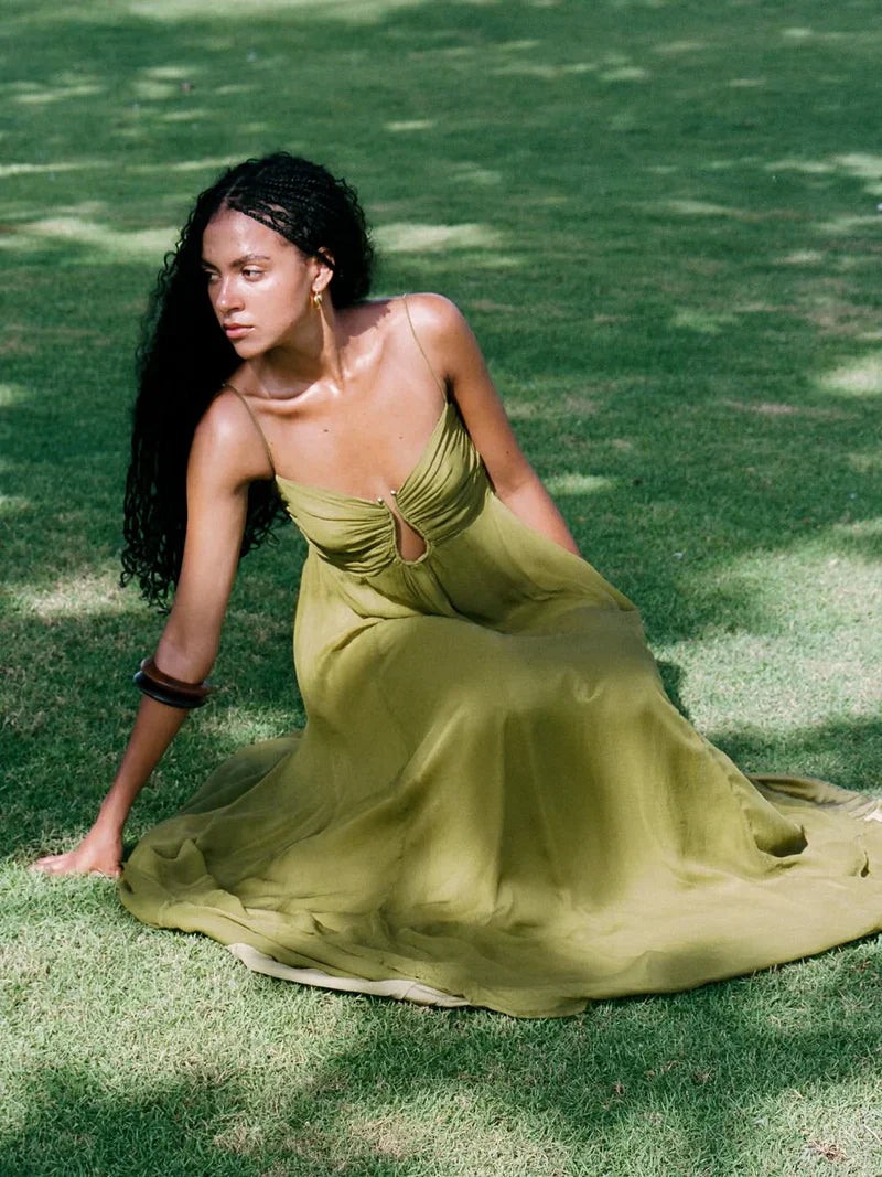 Woman wearing the olive green maxi dress with keyhole bust, sitting gracefully on green grass, looking to the side.