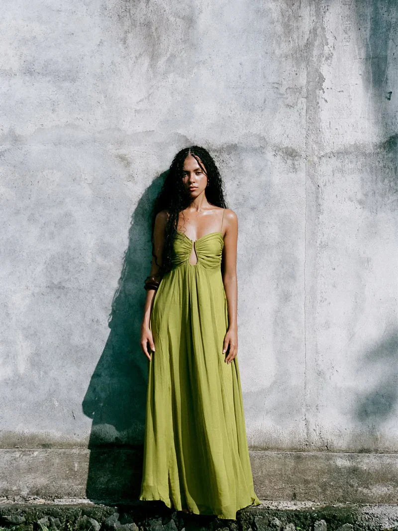 Woman in the olive green maxi dress with keyhole detail, standing against a weathered concrete wall, full body shot.