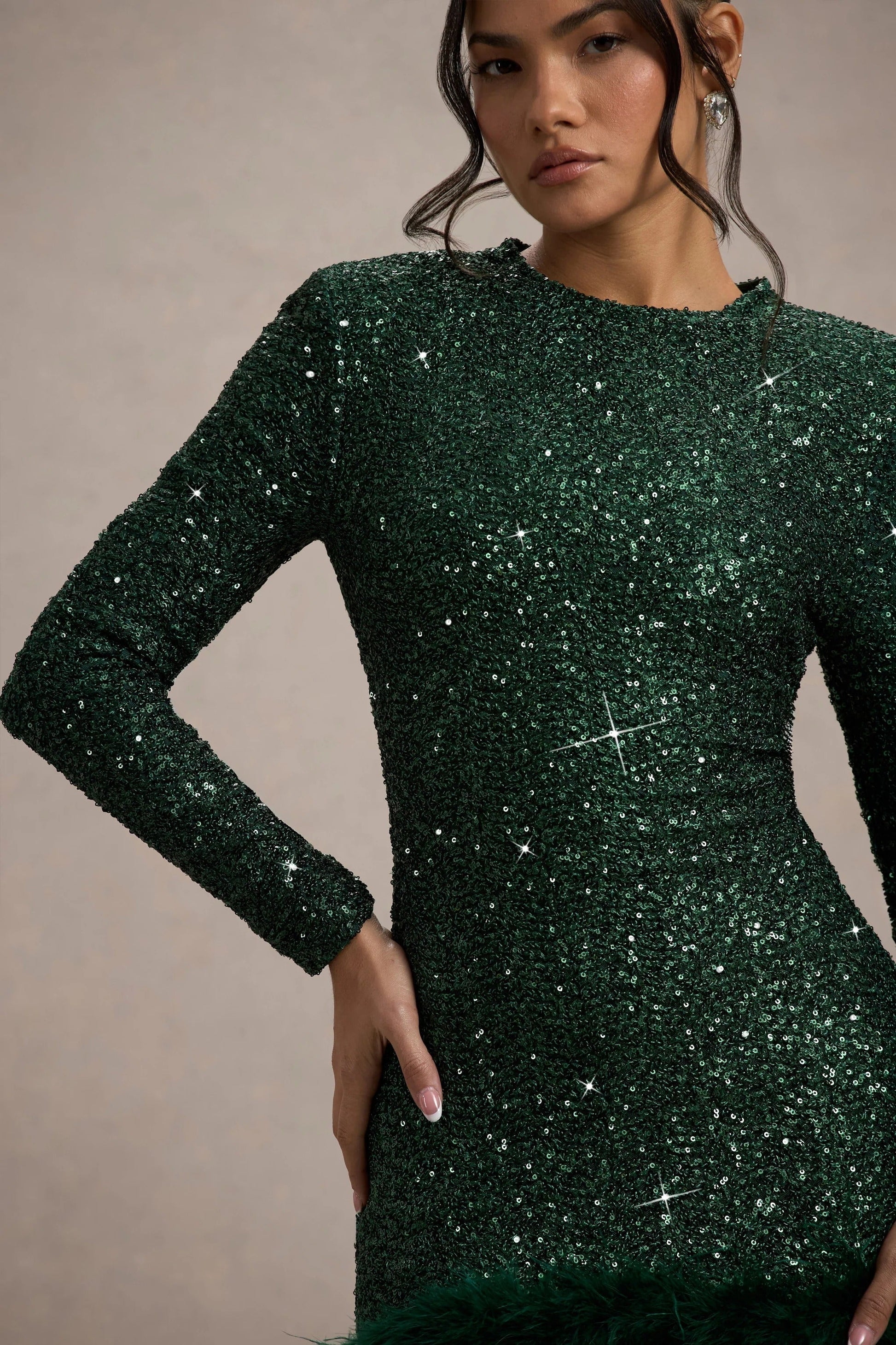 Close-up of the shimmering emerald green sequin fabric of the long-sleeved mini dress, with subtle feather detail.