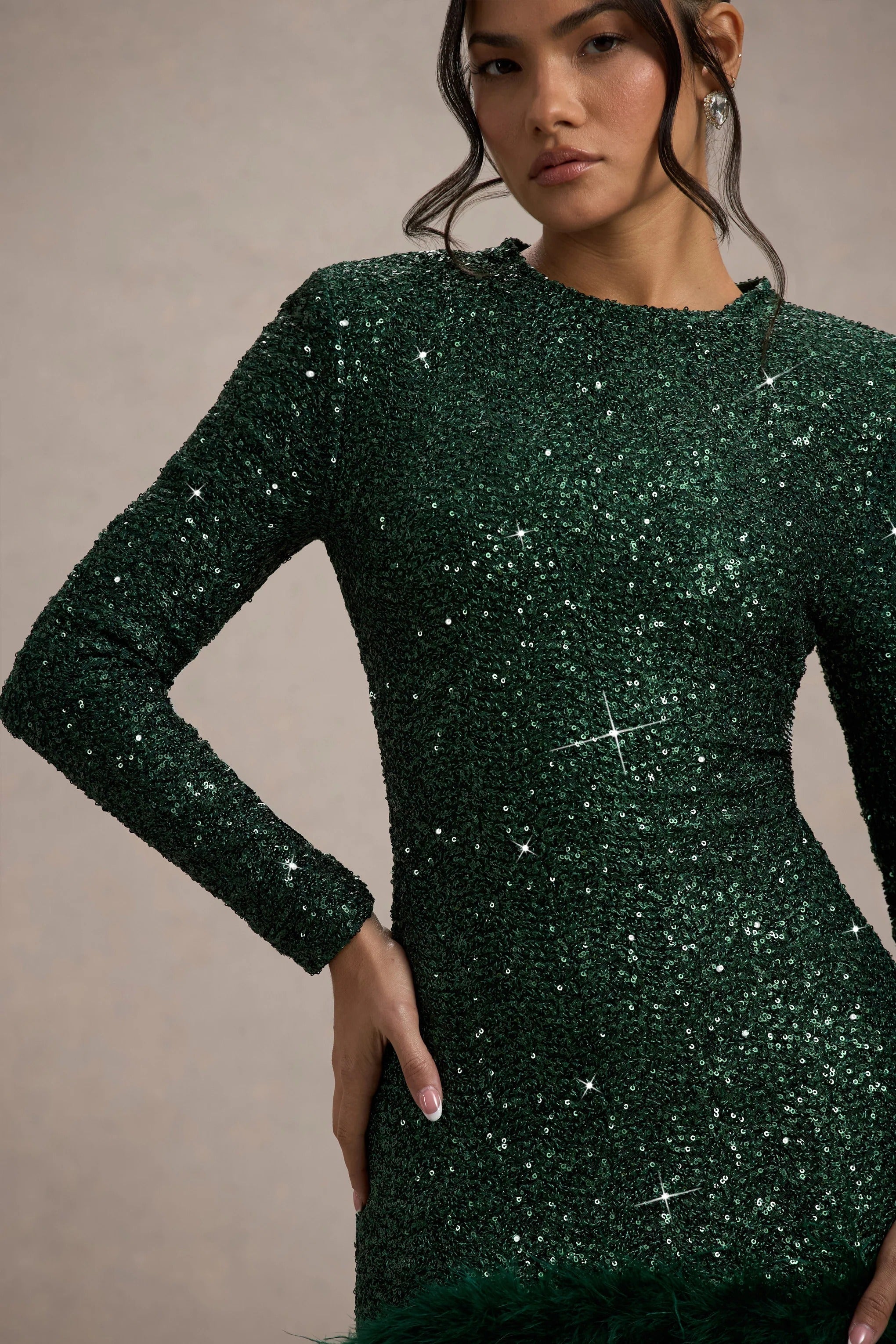Close-up of the shimmering emerald green sequin fabric of the long-sleeved mini dress, with subtle feather detail.