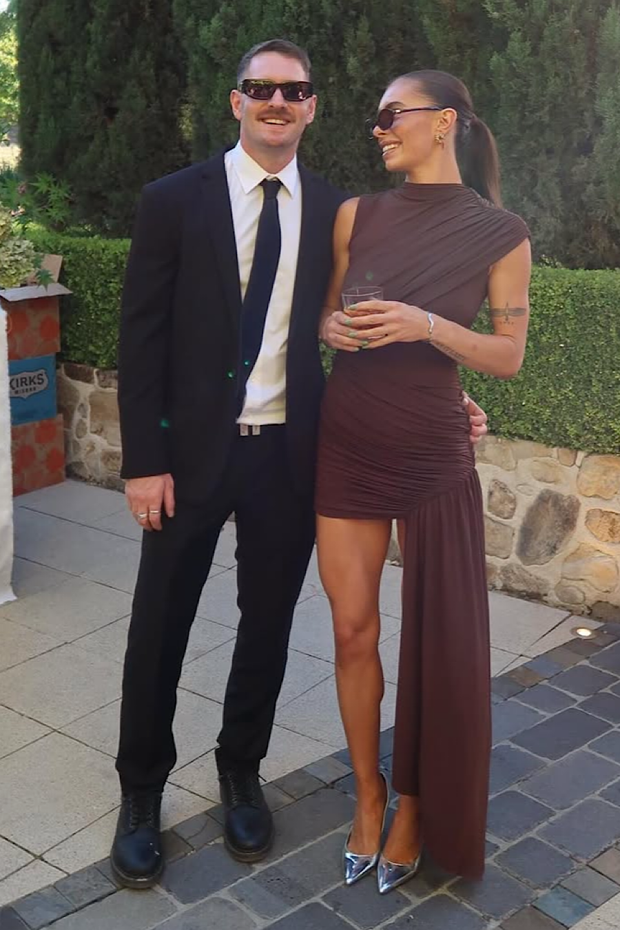 Woman in a brown ruched mini dress with silver heels standing next to a man in a black suit and tie.