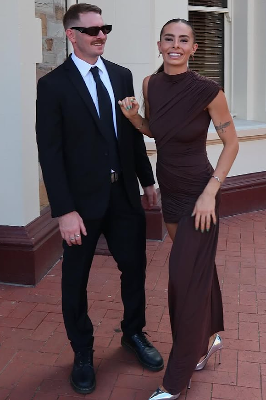 Woman smiling in a brown ruched mini dress with a man in a black suit, showing the dress's movement.