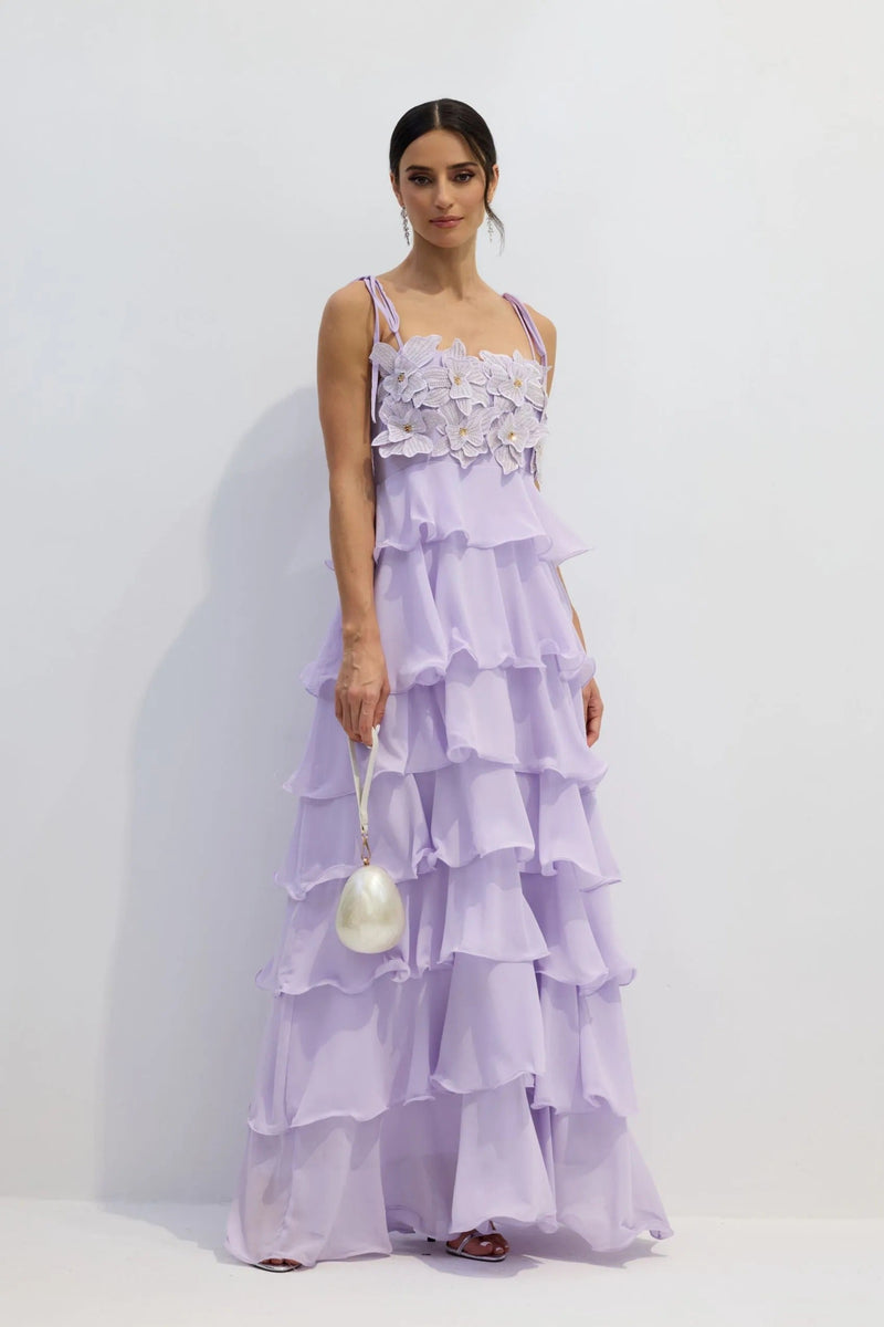 Full-length view of a lavender tiered maxi dress with floral bodice and delicate shoulder ties, paired with a pearl handbag.