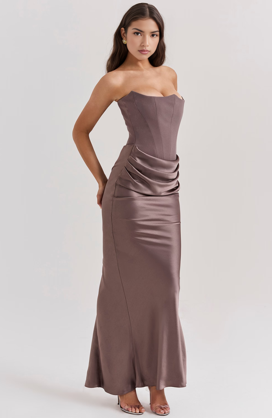 Side profile of a woman wearing a taupe corset maxi dress with a structured bodice and draped skirt, showing the elegant silhouette.