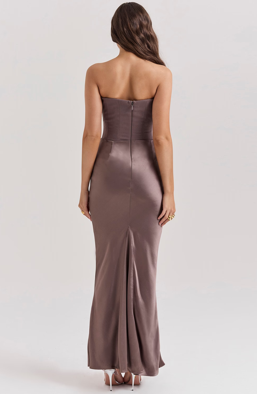 Back view of a taupe corset maxi dress, highlighting the hidden zipper closure and subtle train, worn by a woman with long hair.