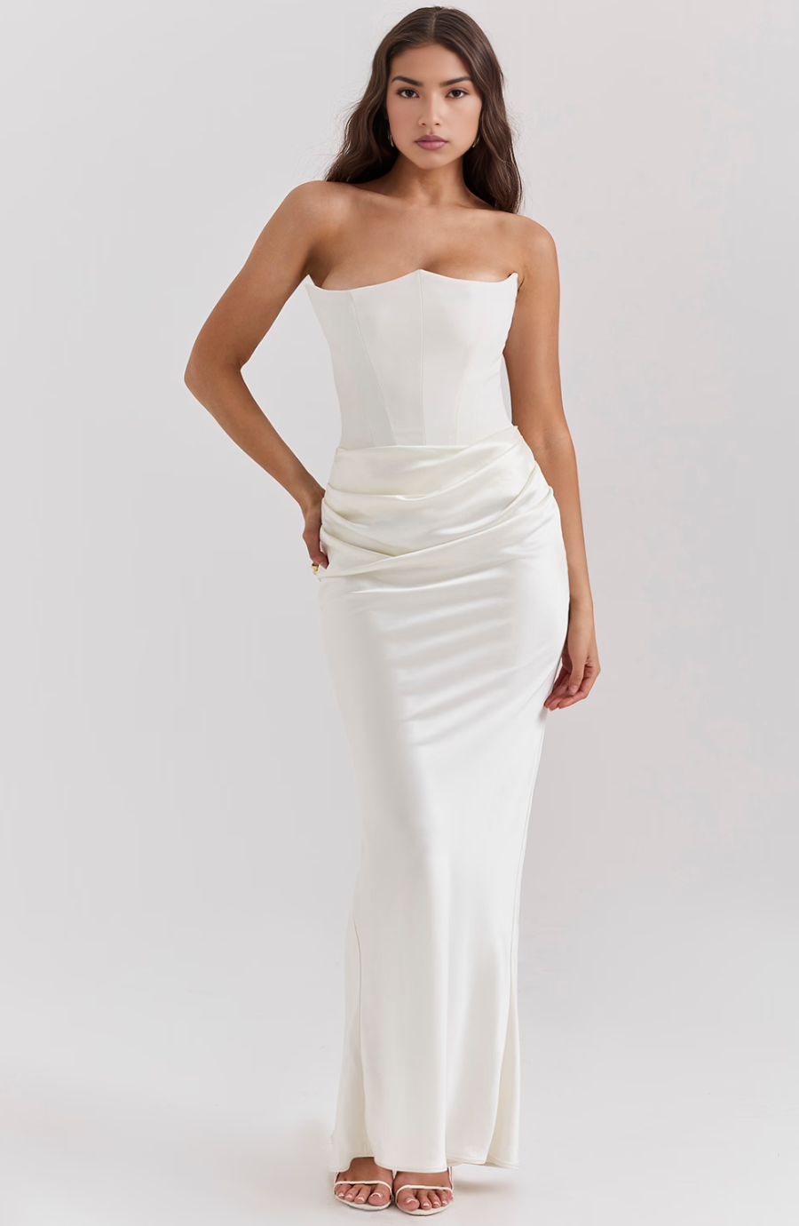 Side view of a woman in a white corset maxi dress, highlighting the fitted silhouette and the elegant drape of the skirt.