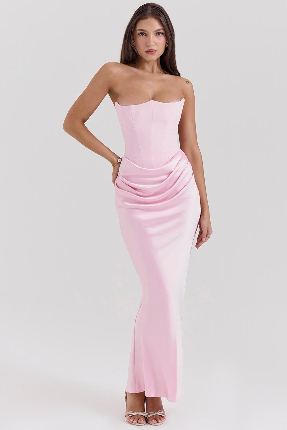 Blonde woman posing in a light pink strapless corset maxi dress with draped detailing and a sweetheart neckline.