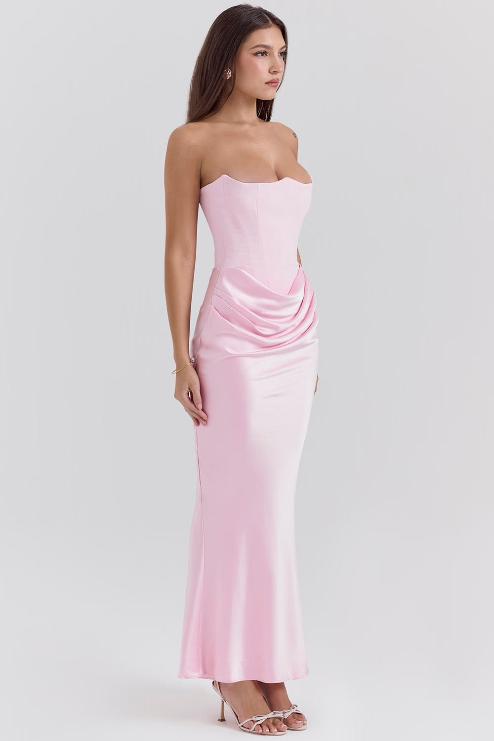 Side profile of a woman in a light pink strapless corset maxi dress, highlighting the elegant drape and form-fitting silhouette.