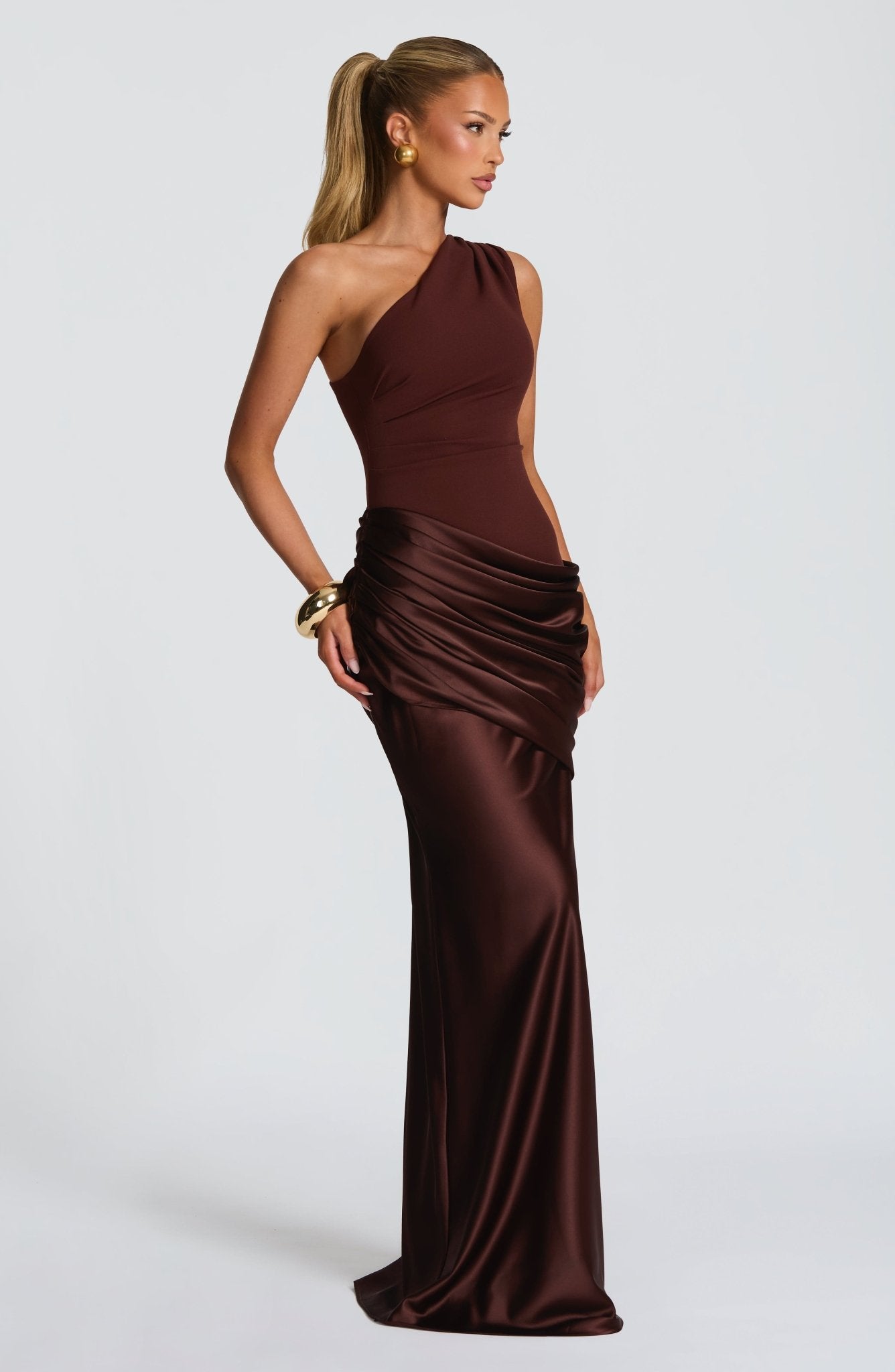 Side profile of the brown Isabelle Draped Maxi Dress, highlighting the unique one-shoulder neckline and ruched satin skirt.