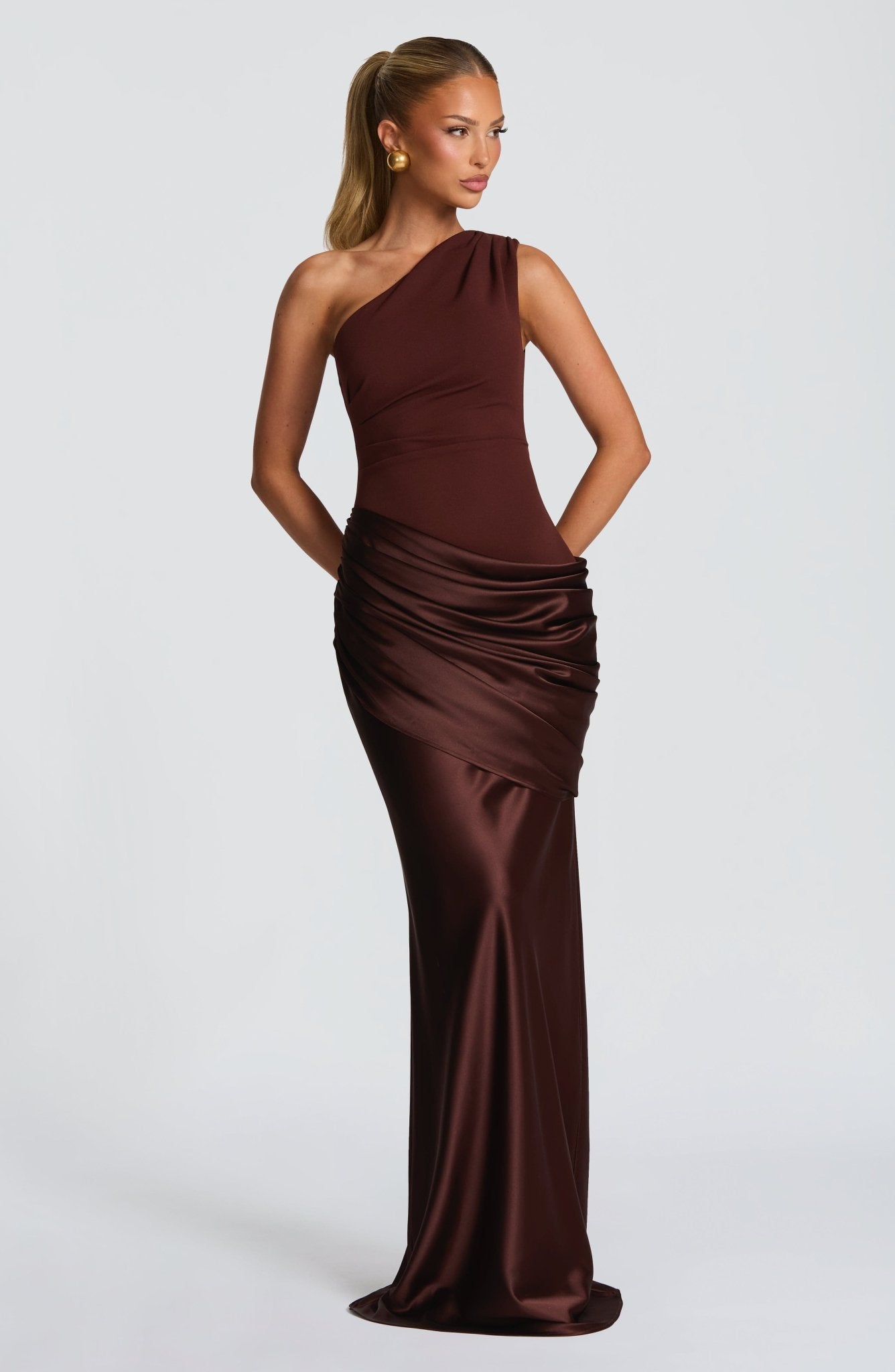 Front view of the brown Isabelle Draped Maxi Dress, with hands clasped behind, emphasizing the fitted bodice and flowing skirt.