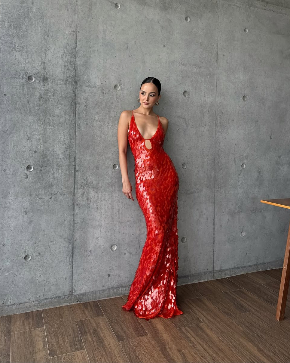 Jacqueline sequin maxi dress in a vibrant red, with a deep v-neck and bodice cut-out, against a concrete wall.